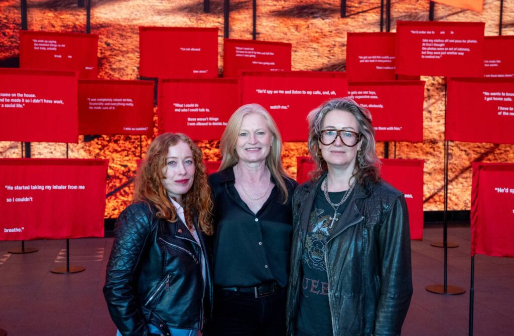 Victoria Yeates, Hetti Barkworth-Nanton and Lorien Haynes stood in front of Refuge's 'No Red Flag is Too Small' exhibition