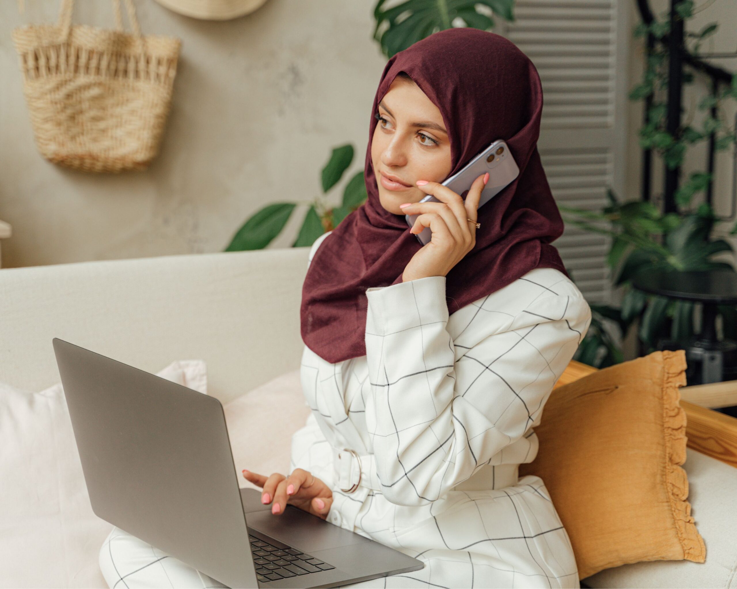 Woman in a hijab sat on her laptop and on the phone
