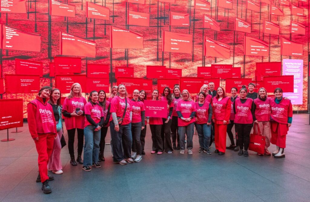 Group photo of volunteers on wearing Refuge t shirts in front of the No Red Flag is Too Small exhibition