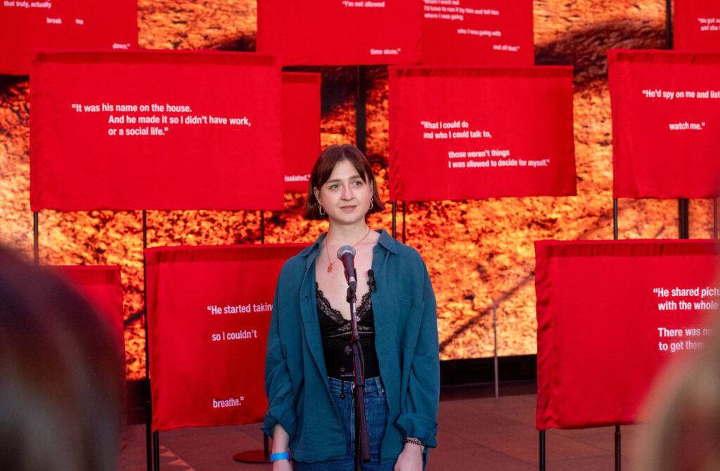 Mid shot of Caitlin O'Ryan stood with a mic in front of red flags