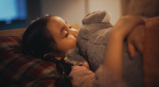Young female child over around 4 years old, laying on bed hugging her elephant toy