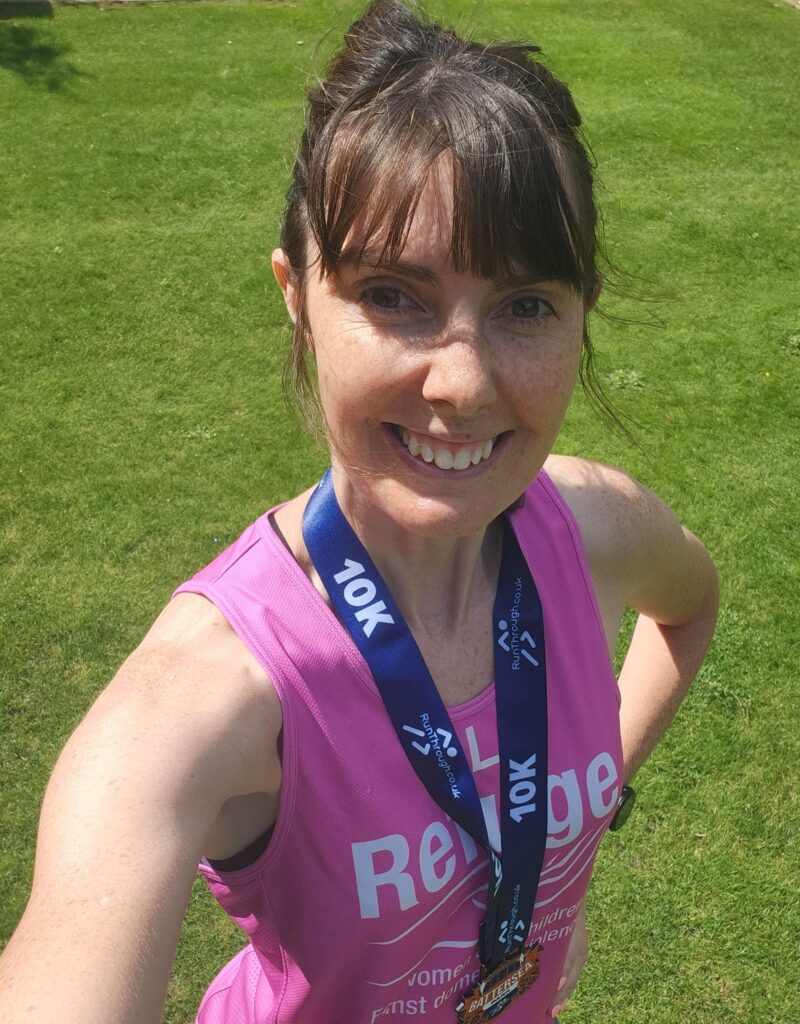 Selfie of Alison May smiling at the camera in a Refuge running vest wearing a medal