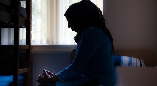 The silhouette of a woman sitting with her head down in a bedroom.