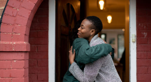 To women hug in door way, they look happy.