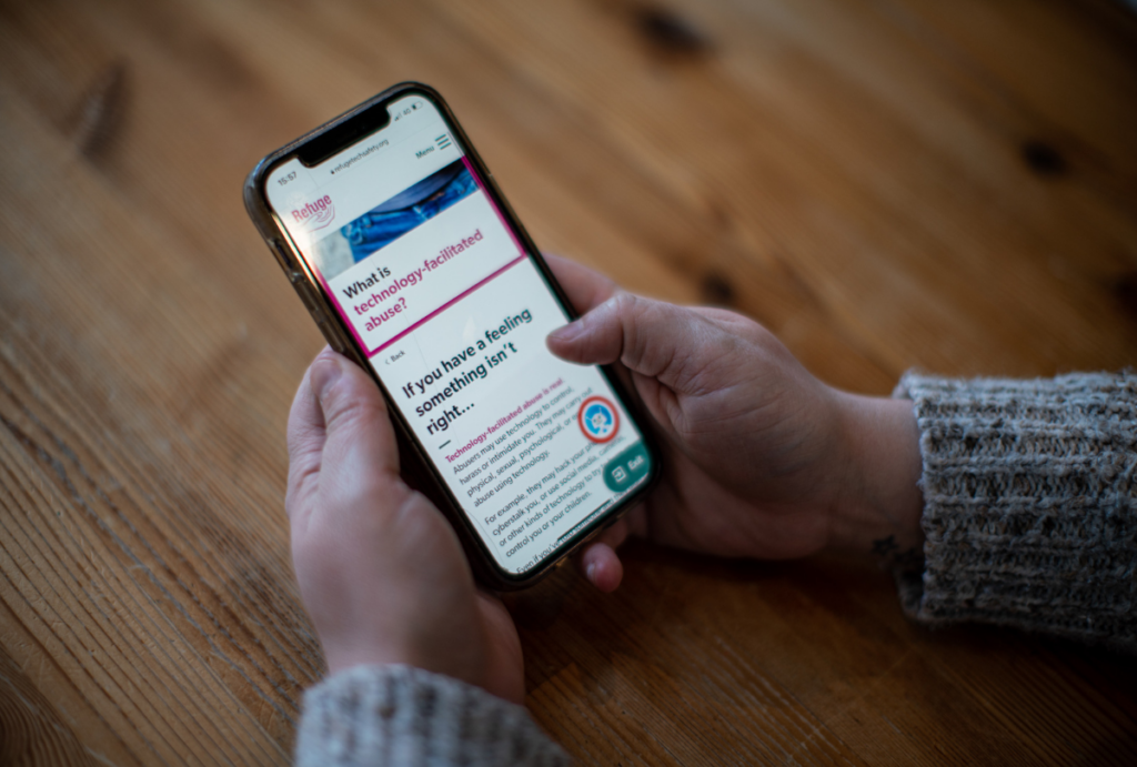 Close up of a hand holding a phone. Webpage displays Refuge's tech Abuse website.