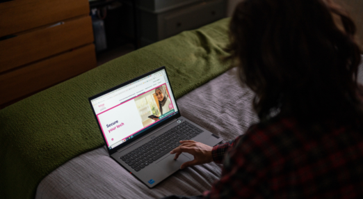 Woman sat on bed with laptop. Webpage shows Refuge's Tech Safety website.
